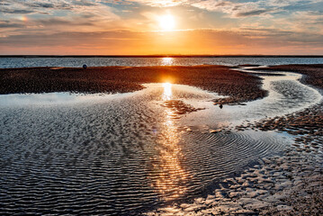 Sonnenuntergang über dem Watt bei Utersum auf der Nordseeinsel Föhr mit der Sonne am Horizont...