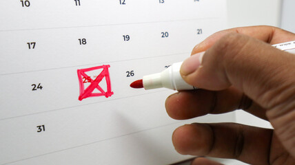A hand uses a red marker to cross out the number 25 on a calendar, representing the concept of a...