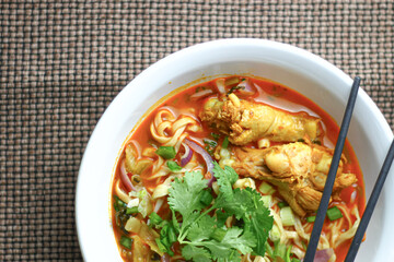 The image shows a bowl of Khao Soi, a traditional Thai noodle curry with chicken, crispy noodles, fresh cilantro, lime wedges, and pickled greens. The dish is beautifully arranged and vibrant.