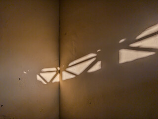 Abstract shadow pattern cast by window blinds creating geometric shapes on corner wall. Natural...