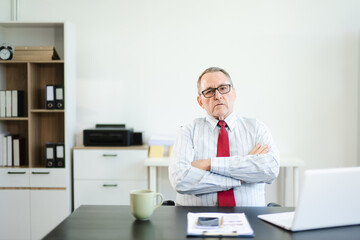 Frustrated senior businessman with smartphone gestures in confusion at office desk, reacting to bad news, tech issue, or business problem with laptop and reports.
