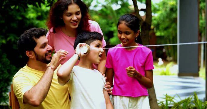 Indian family playing with string telephone in home garden, enjoying creative outdoor activity, spending quality fun time together with kids, parents, siblings, smiling and bonding joyfully
