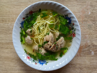 Traditional bowl of meatball with green vegetables and meat served in clear broth on wooden table