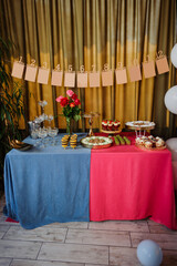 A stylish dessert table for a baby's first year celebration features a banner with month markers, a variety of sweets, and elegant pink and blue tablecloths