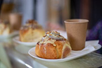 Sinabon bun with cream, nuts and aromatic coffee in a paper cup against the background of a craft...