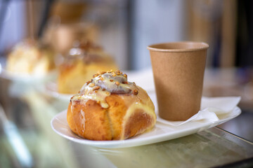Sinabon bun with cream, nuts and aromatic coffee in a paper cup against the background of a craft...