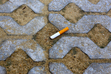 A discarded cigarette butt lying on a sandy pavement surface.