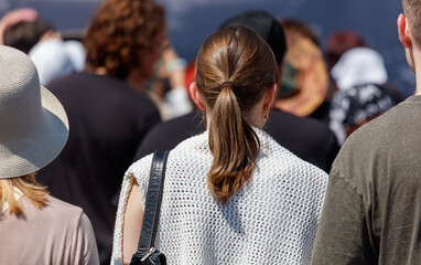 A woman with a ponytail and a white shirt is standing in a crowd of people