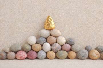 Stacked stone pyramid with smooth pebbles and golden stone on top, arranged on neutral fabric background, creating calm and balanced atmosphere