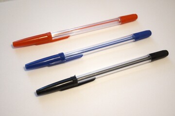 Three pens – red, black, and blue – arranged on a white background. Stationery concept with...