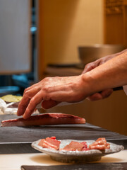 A chef skillfully prepares sashimi, showcasing fresh fish on a cutting board, with delicate pieces elegantly arranged on a Kobe Wagyu beef plate nearby in Omakase Japanese restaurant