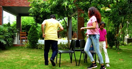 Indian family playing musical chair game in home garden while laughing and bonding, spending fun quality time together outdoors during weekend with joyful moments, sport, and entertainment