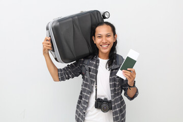 Asian male traveler wearing casual clothes, backpack, camera on neck, carrying suitcase on...