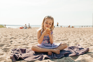 Young girl enjoying ice cream while sitting on the beach on a sunny day