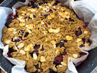Baked plum cake with grated spelt dough and almond flakes in round baking pan on wooden table.