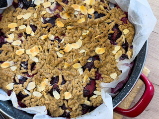 Baked plum cake with grated spelt dough and almond flakes in round baking pan on wooden table.