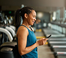 Portrait of a young black woman using a phone ant exting taking a break exercising in a gym,...