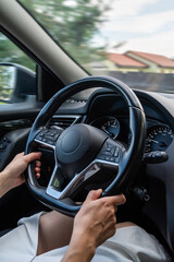 Hands gripping steering wheel while driving through suburban neighborhood on a sunny day