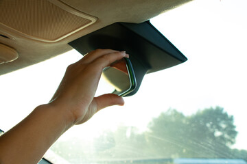Female hand adjusting rearview mirror in car against sunlight through windshield