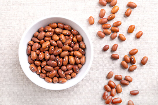 Dutch brown beans in a white bowl on linen. Bruine bonen in Dutch, a dried variety of bean, Phaseolus vulgaris. Oval shaped and caramel brown in color. Used for baking, boiling, or in soups and stews.
