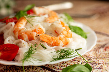rice noodles with shrimp and tomato slices on a wooden table