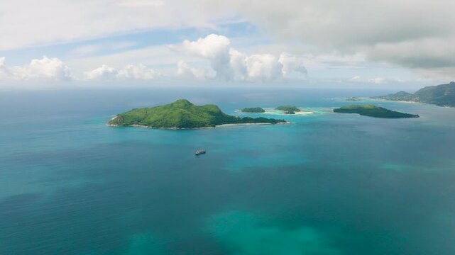 Ocean with a ship and a green island in the distance under a partly cloudy sky. Seychelles, Mahe. Ile au cerf island.