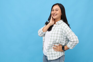 Smiling and attractive Asian woman looking at camera posing on blue background, copy space, fashion model standing in studio, advertising concept.