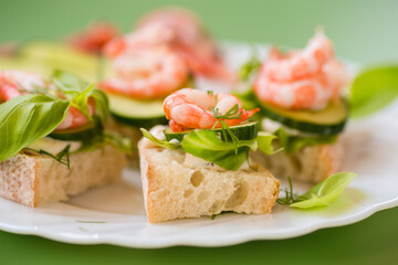 Delicious portioned appetizers with shrimps and greens on a green background