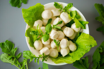 Mini mozzarella balls with herbs in white bowl on grey background