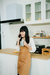 Asian woman chats on the phone and drinks coffee in a cozy kitchen with fresh vegetables. A vibrant lifestyle scene perfect for food, wellness, and communication concepts.