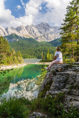 Woman sitting on rock overlooking Eibsee lake and Bavarian Alps in Germany. Serene alpine...
