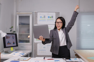 Excited businesswoman celebrating success with laptop in office
