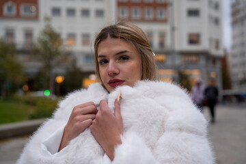 Elegant woman wearing white fur coat in urban setting