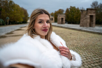 Influencer taking selfie wearing white fur coat in the temple of debod, madrid