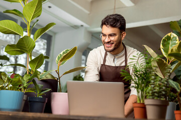 Male shop assistant in the flower shop working on a laptop