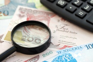 Nigerian naira currency money bills and calculator with magnifying glass. The concept of taxation and money count