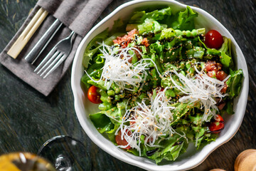 Fresh vegetable salad with cherry tomatoes, shredded daikon, sesame seeds, and dressing in a white...