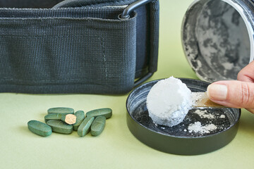 Tablets and spoon of creatine powder on green background. Sports supplements.