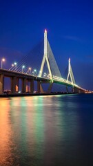 Obraz premium Illuminated cable-stayed bridge spans waterway at twilight, reflecting lights onto calm water