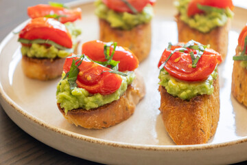 avocado crostini topped with roasted cherry tomatoes and fresh basil, served as a bite-sized party appetizer. Perfect for food blogs, entertaining ideas