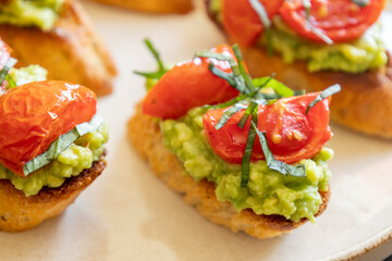 avocado crostini topped with roasted cherry tomatoes and fresh basil, served as a bite-sized party appetizer. Perfect for food blogs, entertaining ideas