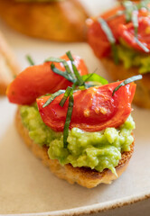 avocado crostini topped with roasted cherry tomatoes and fresh basil, served as a bite-sized party appetizer. Perfect for food blogs, entertaining ideas