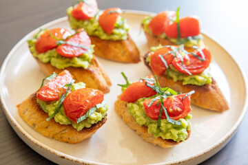 avocado crostini topped with roasted cherry tomatoes and fresh basil, served as a bite-sized party appetizer. Perfect for food blogs, entertaining ideas