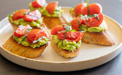 avocado crostini topped with roasted cherry tomatoes and fresh basil, served as a bite-sized party appetizer. Perfect for food blogs, entertaining ideas