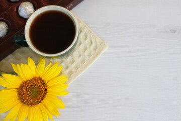 a box of chocolates with a cup of coffee and a small sunflower early in the morning