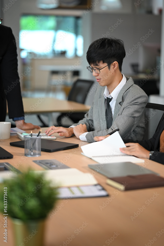 Poster focused businessman reviewing data and making calculations at a collaborative workspace