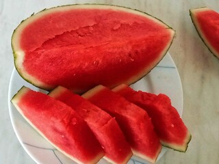 A cut watermelon. On a white plate lie several slices of bright red watermelon flesh, and next to...