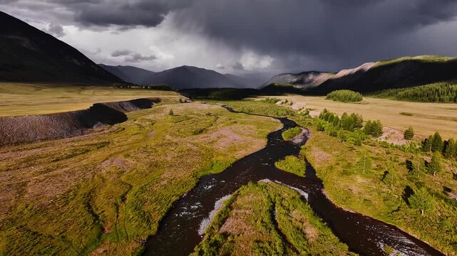 Meandering stream and river against the backdrop of mountains and clouds on the Ukok plateau, Altai Republic. Drone and aerial view. Nature, natural places. Village life.