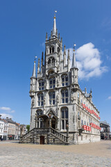 Fototapeta premium The magnificent Gothic town hall of Gouda stands prominently in the market square under a bright blue sky with a few clouds.
