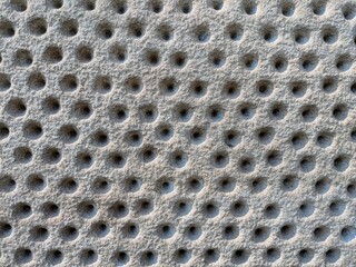A unique, full-frame texture of a rough stone surface with a repeating pattern of small, circular...